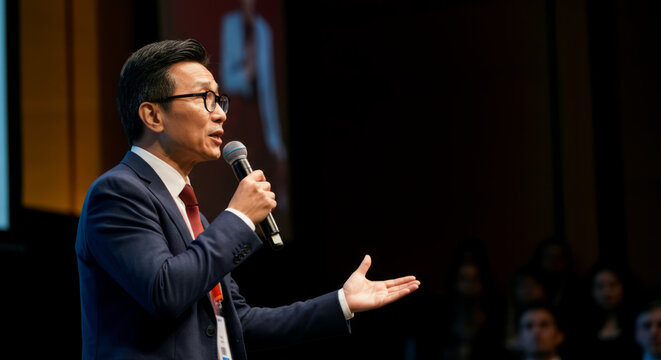 Asian male speaker in business suit delivering presentation at conference