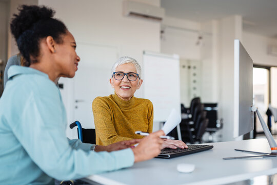 Business woman in wheelchair working with colleague in modern inclusive office. Diversity, support