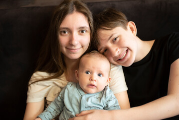 Family photo of children. Two brothers and sister hugging on sofa, two teenagers and baby sitting together at home.