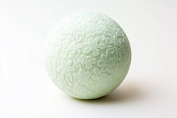 A pale green sphere adorned with an embossed floral pattern, possibly decorative or artisanal.