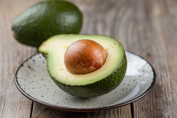 Fresh avocado half with seed on handmade ceramic plate placed on rustic wooden surface