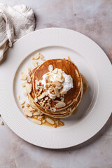 Stack of vegan pancakes with cream, syrup and nuts.