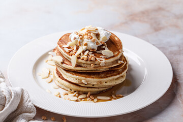 Stack of vegan pancakes with cream, syrup and nuts.