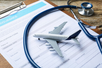 Medical tourism. Travel insurance application form, stethoscope and plane model on wooden table,...