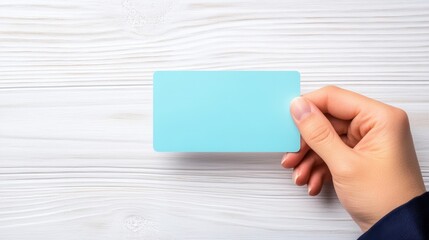 Obraz premium A hand holds a blue card over a light wooden surface, suggesting themes of identity, membership, or payment.