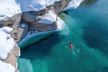 A stunning aerial view of a person diving into icy turquoise waters, framed by snow-covered cliffs, showcasing the thrill of winter swimming against nature's backdrop.