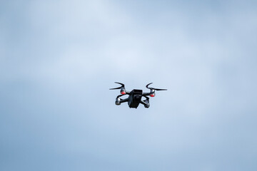 A dark-colored drone is captured mid-flight against a gray, overcast sky, showcasing its compact design and aerial capabilities.