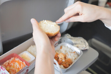 Airplane lunch close up: Womens hands butter a bun with a knife, Close-up of a womans hands buttering a bun with a knife during an airplane lunch, showcasing in flight dining and meal preparation