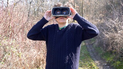 10 year old boy with 3d AI virtual reality headset viewer in nature immerses himself in an immersive visual experience with reality augmented by artificial intelligence