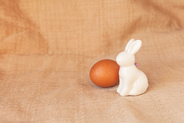 Happy easter decoration with white bunny decorative statuette and colorful eggs on eco textille background. Minimal festive composition, natural farm lifestyle. Copy space, place for text, front view