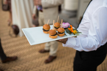 tray of mini hamburgers being served by caterer at elegant outdoor summer wedding