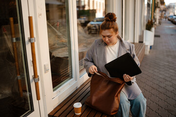 A White woman in her late 20s, wearing a grey blazer and jeans, is sitting on a wooden bench...