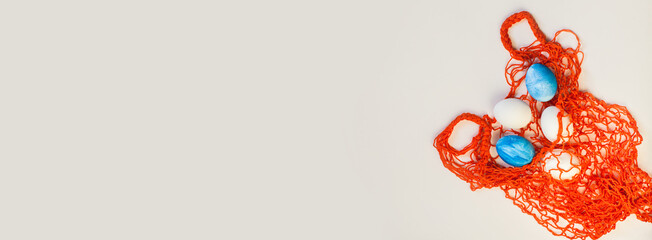 Mesh shopping eco bag, white and blue eggs on white or gray background. Easter holiday greeting card concept. Cotton knitted eco-friendly zero waste shopper. Flat lay, top view, place for text, banner