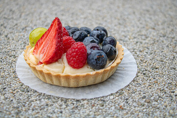 Side view of a sweet tart with fruit and cream with half a strawberry, blueberries and raspberries lying on top of the cream, covered with a clear glossy syrup
