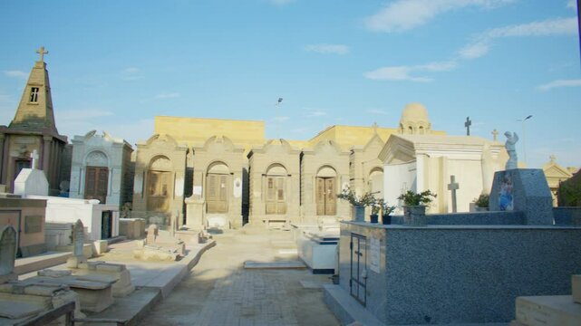 A sunlit cemetery with rows of elaborate mausoleums, ornate wooden doors, and stone crosses. Overview of a Coptic cemetery in Old Cairo.