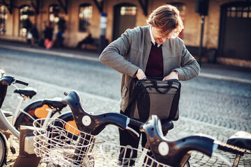 Mature man picking up a bicycle from the public bicycle sharing station in the city