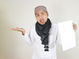 handsome asian muslim man wearing black turban or shemagh holding blank white paper and showing...