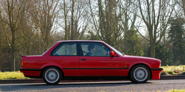 Stony Stratford,UK - Mar. 2nd 2025:  1990 red BMW 318  classic car driving on a British road.