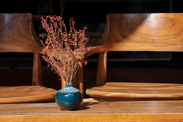 selective focus red-orange dried flowers in a blue indigo ceramic vase on a brown wooden table with...