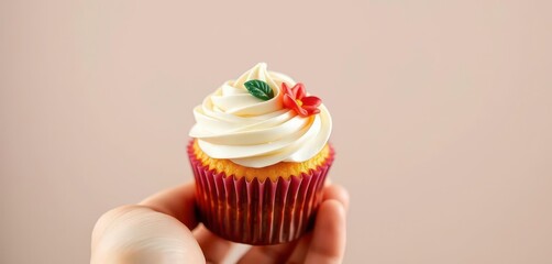 A delicately decorated cupcake held gently in a hand, frosting, strawberry