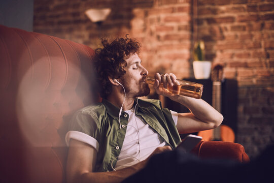 Man relaxing on couch drinking beer and listening to music