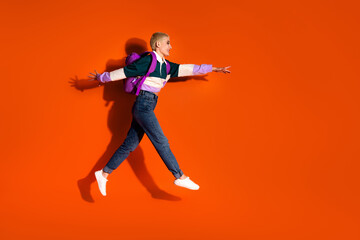 Cheerful Young Woman Jumping Against an Orange Background with Casual Fashion and a Bright Smile