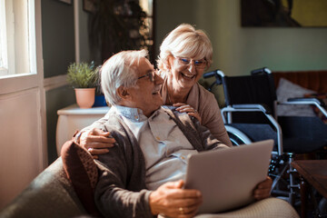 Elderly couple embracing while using laptop at home