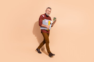 Confident Gray-Haired Man Holding Documents and Coffee in Stylish Attire Against a Solid Beige Background