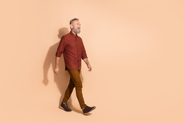 Fototapeta premium Middle-aged man in casual attire walking confidently against a beige background, showcasing modern fashion and leisure.