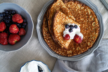 Homemade pancakes with fresh berries and cream on a rustic table setting
