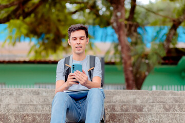 Obraz premium University student using a smartphone to get study help from an AI assistant. Young man sitting on outdoor stairs with a backpack, engaged in online learning.