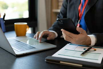 A man in a suit is working on documents in an office. He holds a pen and is analyzing data. This scene conveys a professional working atmosphere.
