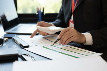 A man in a suit is working on documents in an office. He holds a pen and is analyzing data. This scene conveys a professional working atmosphere.
