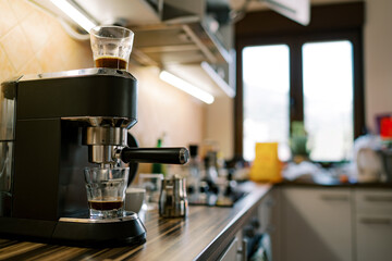 Black coffee dripping from a carob coffee maker into a glass on a stand