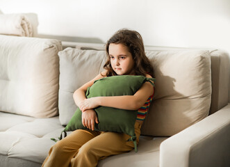 Obraz premium Child sitting alone on sofa feeling stressed unhappy, sad and depress. Little girl embracing pillow.