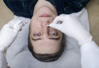 Man undergoing facial cleansing and blackhead removal. Beautician using comedone extractor or uno...