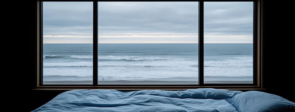 Fototapeta A serene view of ocean waves crashing against the shore can be seen from a cozy bedroom, complete with soft, inviting bedding, on a cloudy morning by the beach