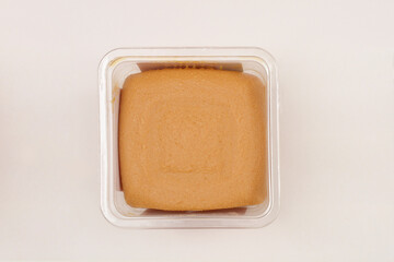 A square block of miso paste is presented in a clear plastic container