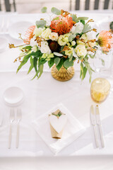Bouquet of flowers stands on a festive table near an invitation with a paper heart on a napkin
