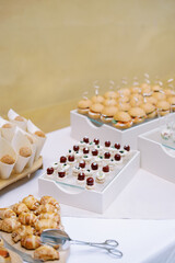 Croissants lie on a wooden board next to small cakes on a stand and mini burgers on a buffet
