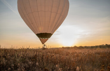 A hot air balloon takes off in a field at sunset