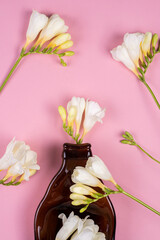 white freesia flowers lying on a flattened glass bottle, soft pink background, international...