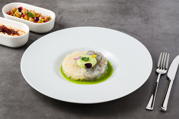 Gourmet shrimp and white fish tartare with avocado mousse, edible flowers, and green sauce, served on a white plate