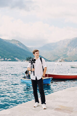 Fototapeta premium Photographer with a camera on a tripod stands on a pier by the sea and looks into the distance