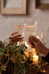 Two hands with glasses of champagne on a background of candles