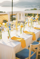 Long festive table with bouquets of flowers and yellow napkins on plates