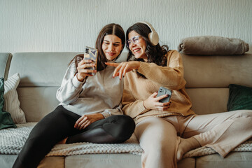 Obraz premium Young caucasian woman and her sister use phone and have fun on couch