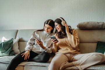 Young caucasian woman and her sister use phone and have fun on couch