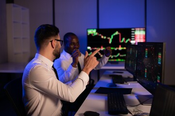 Two businessmen, financial analysts or investment advisers sitting at office desk with copmputers...