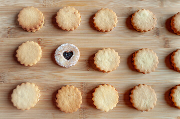 Homemade round shortbread cookies placed in a rows on bamboo plank. One of them is different.